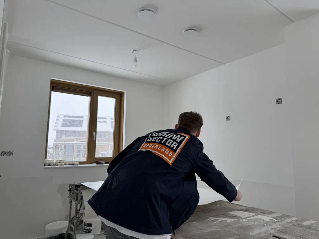 Behanger van Bouwsector Nederland in werkjas legt een baan renovlies op de plaktafel in een witte nieuwbouwkamer