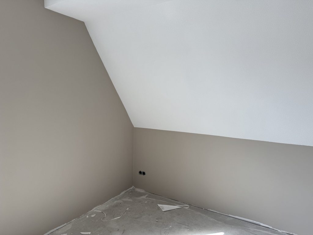 Zolderkamer met een schuine wand wit afgewerkt en de rechte wanden in een zachte taupe gesausd