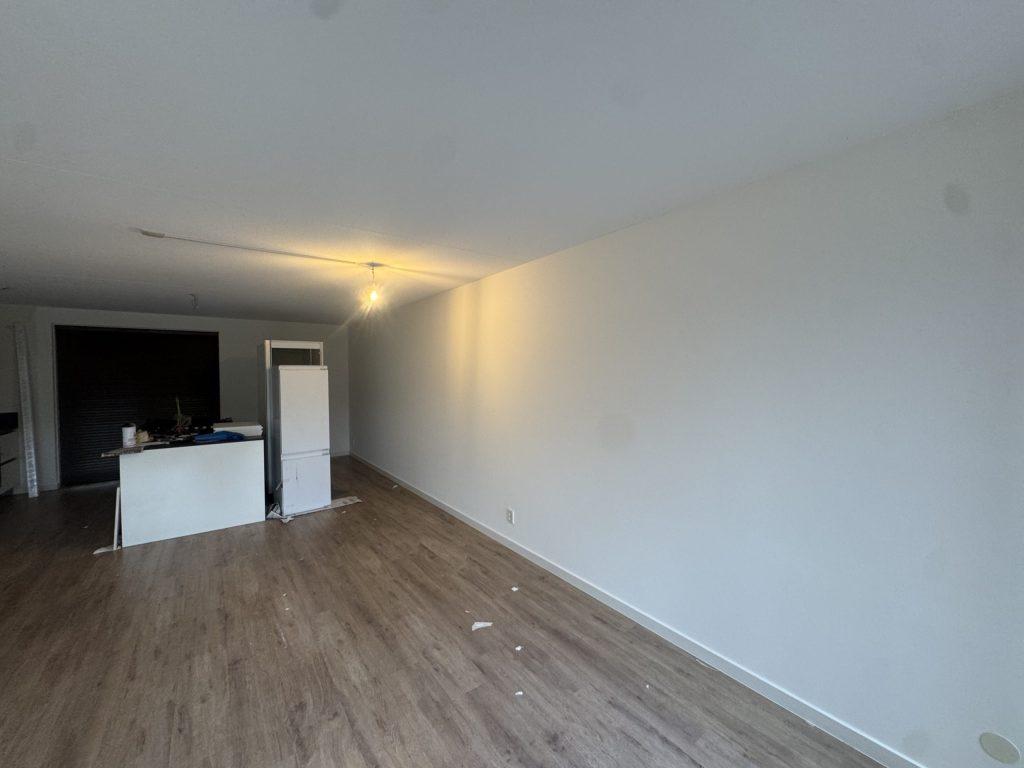 Lange wit gesausde wand in een nieuw appartement met laminaat en een keukenblok achterin